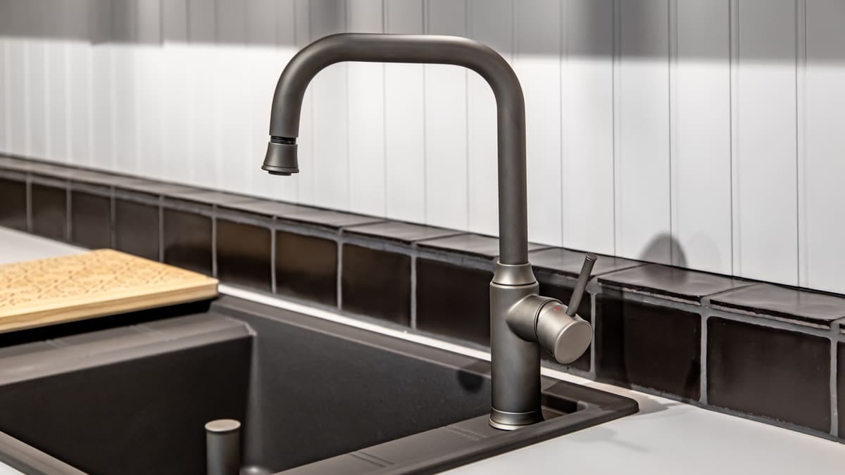 Torneira cromada de cozinha com bica alta instalada sobre uma pia de inox, com água corrente