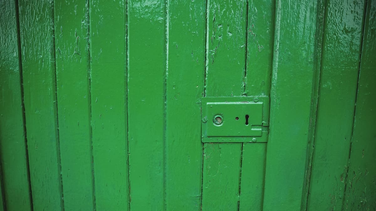 Chave de fenda apertando o parafuso de uma dobradiça de porta de madeira, com o batente ao fundo